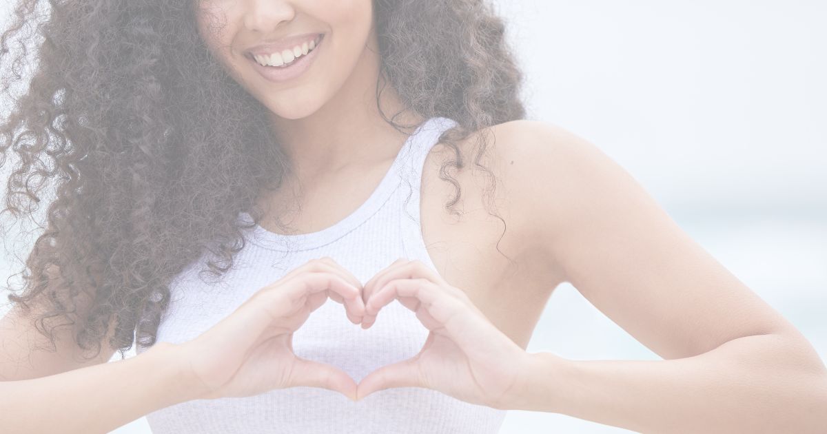 Smiling woman forming heart shape with hands representing wellness energy balance and natural lifestyle.